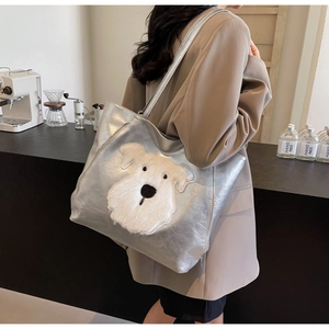 Detailed close-up of a silver metallic tote bag featuring a plush schnauzer puppy embroidery