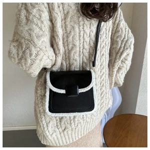 Détail du petit sac carré vintage avec bordure pelucheuse porté sur un pull en maille torsadée