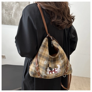 Rear view of model wearing a plaid canvas tote bag with embroidered cartoon dog and leather strap