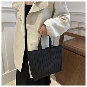 Close-up of black pleated tote bag with glossy handles on a beige trench coat