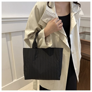 Detail view of black quilted tote bag with vertical pleated texture and glossy finish