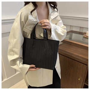 Detail of black quilted tote bag with pleated fabric texture and leather handle