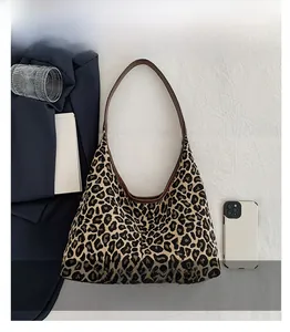 Detail of leopard print knit underarm bag with premium brown leather strap on textured fabric