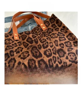 Detail of leopard print tote bag featuring brown leather handles and gold rivet accents