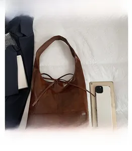 Brown leather tote bag size comparison with tablet and phone on white fabric
