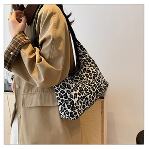 Detail view of large leopard print tote bag with black strap on model in khaki coat