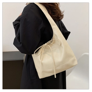 Detail of a creamy white tote bag featuring a bow tie ornament shown on a model's shoulder