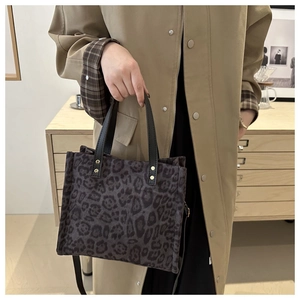 Detail of dark leopard print tote bag featuring black leather handles and gold rivet studs