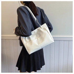 Close-up of a white leather tote bag with silver chain straps shown on a model
