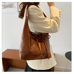 Detail of caramel brown PU leather hobo bag with side drawstring bow accent on model