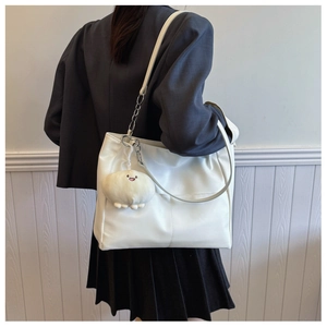 Close-up of white tote bag with chain strap and plush pendant on textured PU leather