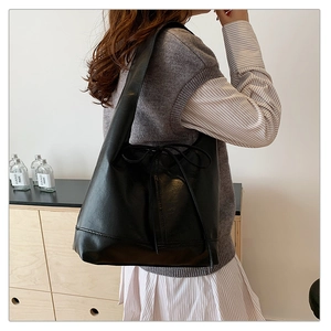 Detailed view of black PU leather tote bag with drawstring bow on a shoulder model