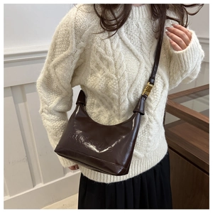 Close-up of brown patent leather tote with Maison embossing and gold buckle on strap