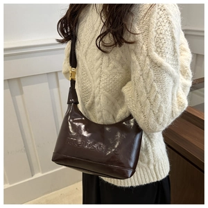 Detail of dark brown glossy hobo bag with maison embossing and golden buckle on shoulder strap