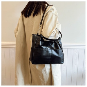 Minimalist black tote bag detail with leather and silver chain strap on model shoulder