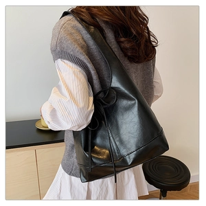 Detail of a black leather shoulder bag with a decorative bow tied on the side strap