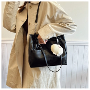 Detail of black faux leather tote bag with silver chain strap and plush mascot charm