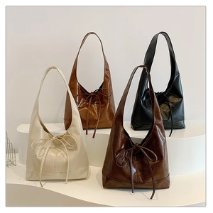 Minimalist tote bag with bow detail in four colors shown on white tiered pedestals