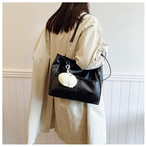 Detail of a large black faux leather tote bag with elegant stitching and plush charm