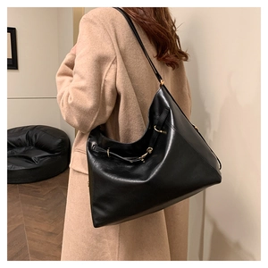 Side view of black leather hobo bag with gold buckle on a model in a camel coat