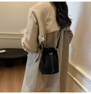 Close-up of a black drawstring bucket bag worn over a classic khaki trench coat