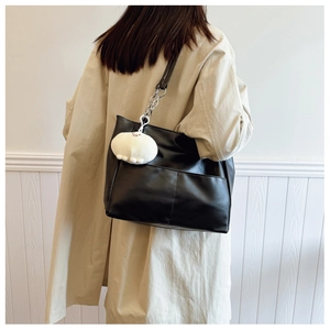 Detail of black faux leather tote bag with white plush charm and chain strap on shoulder