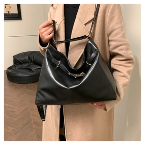 Detail of a large black hobo shoulder bag with glossy leather and golden metal hardware