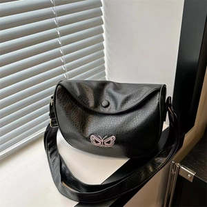 Close-up of black crossbody saddle bag with crackle texture and pink butterfly embroidery