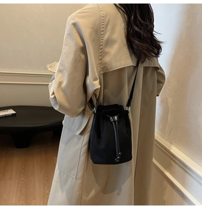 Detail shot of a black drawstring bucket bag worn over a stylish khaki trench coat