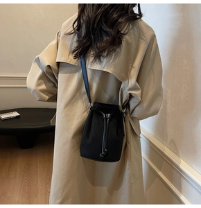 Dettaglio borsa a secchiello nera con coulisse indossata sopra un trench beige