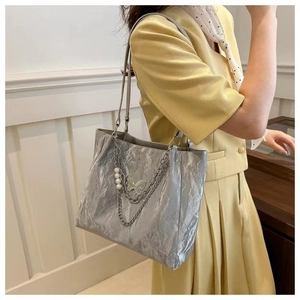 Silver tote bag detail showing metallic butterfly pendant and pearl chain decoration