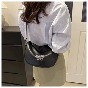 Close-up of black leather crossbody bag with silver butterfly hardware and texture