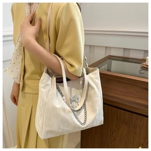 Detail of off-white tote bag featuring silver chain and butterfly ornament on shoulder