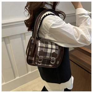 Brown plaid saddle bag with metal buckles shown worn as a shoulder bag in lifestyle setting