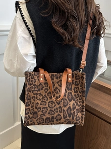 Leopard print tote bag with brown leather straps shown on a model in a stylish setting