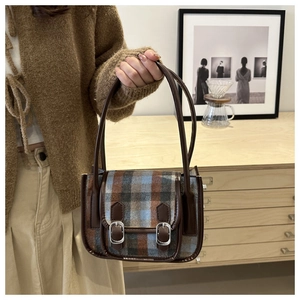 Detailed close-up of retro plaid wool handbag with brown leather straps and metal buckles