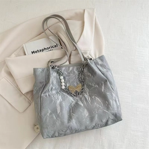 Detail of silver pleated tote bag with pearl and golden butterfly charm on a blazer
