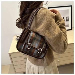 Detail of vintage blue and brown plaid underarm bag with leather buckles on a model