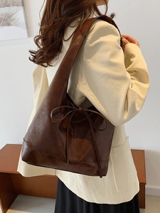 Deep brown retro shoulder bag with bow detail worn by model in minimalist indoor setting