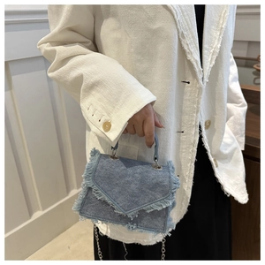 Detail of blue denim shoulder bag featuring fringe edges and silver metal chain strap