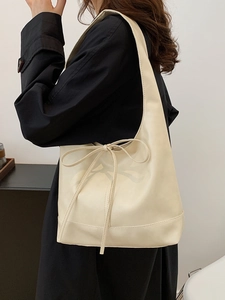 Creamy white oversized tote bag with minimalist bow detail shown on black coat