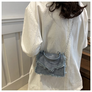 Denim crossbody bag with fringe edges and silver chain strap shown on a model