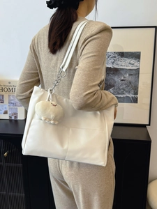 Minimalist white tote bag with chain strap and plush pendant in modern interior setting