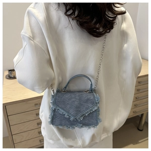 Blue denim crossbody bag with fringe edges and silver chain strap shown on a model