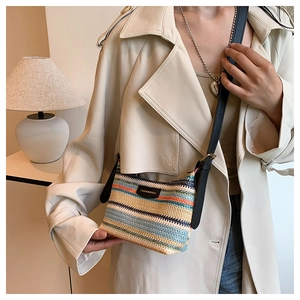 Detail of multi-colored woven straw crossbody bag with leather brand tag and slim strap