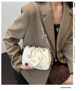 Detail view of white drawstring bucket bag with colorful heart patches and silver chain strap