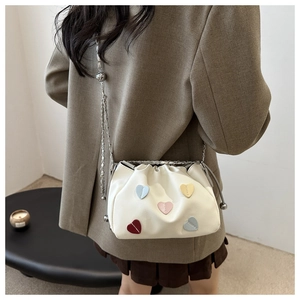 Detail of white leather drawstring bucket bag featuring colorful 3D heart patches and chain