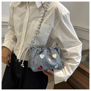 Close-up of blue denim drawstring bucket bag featuring colorful heart patches and silver chain