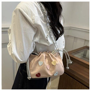 Close-up of pink suede bucket bag with colorful heart patches and silver chain strap