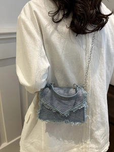 Light blue denim crossbody bag with frayed edges and metal chain strap shown on model